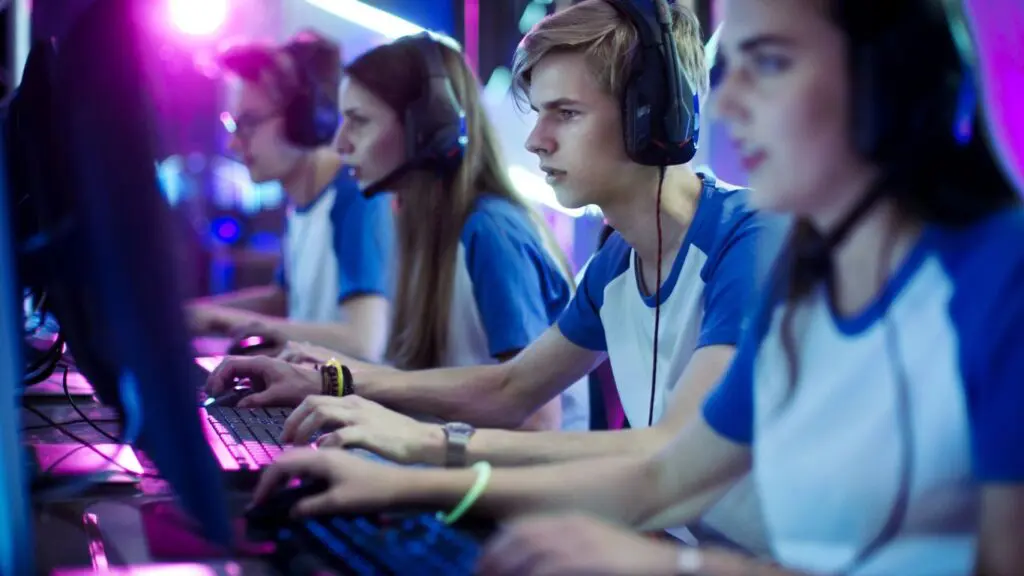Team of young gamers in blue jerseys and headsets competing at computers under neon lights.