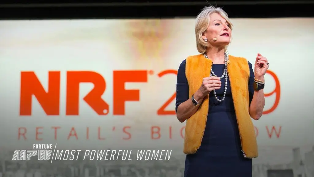 Woman in orange vest speaking on stage at a Fortune Most Powerful Women event.