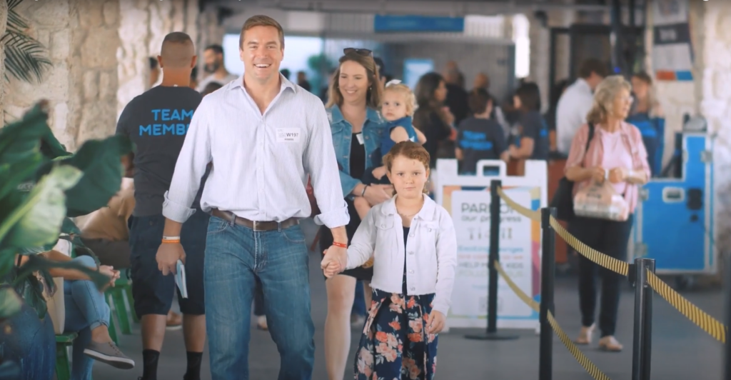 Smiling man walks holding a young girl's hand through a busy venue.