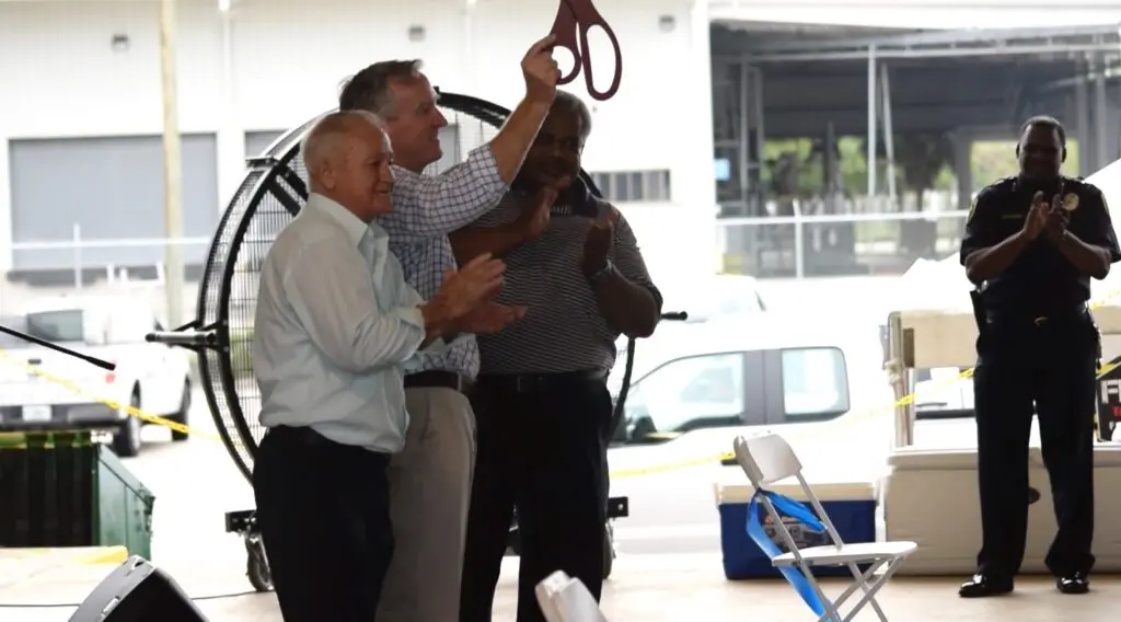 Three men in business casual applaud during a ribbon-cutting ceremony.