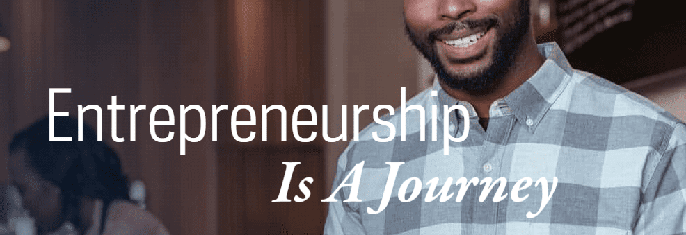 Smiling bearded man in a checkered shirt with text Entrepreneurship Is A Journey.