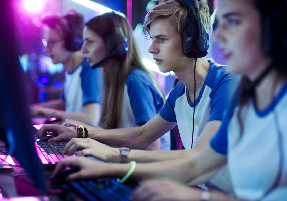 Team of young gamers in blue jerseys and headsets competing at computers under neon lights.